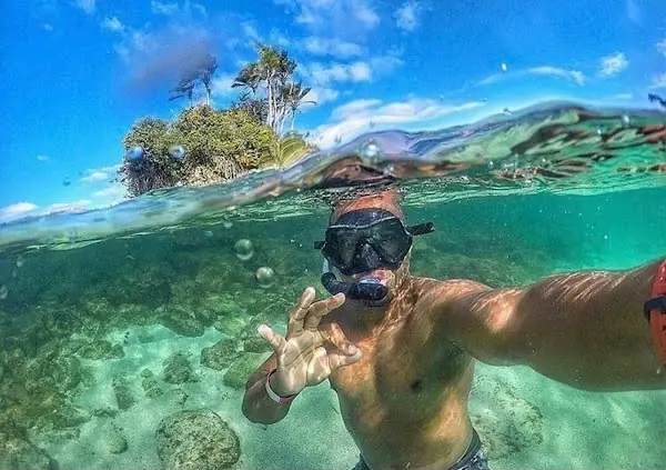 Cliente mergulhando com snorkel em água transparente ao lado de uma ilhota