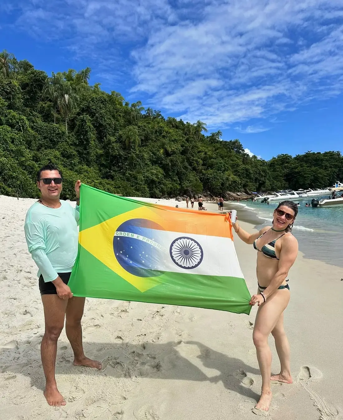 Turistas segurando bandeiras do Brasil e da Índia na praia